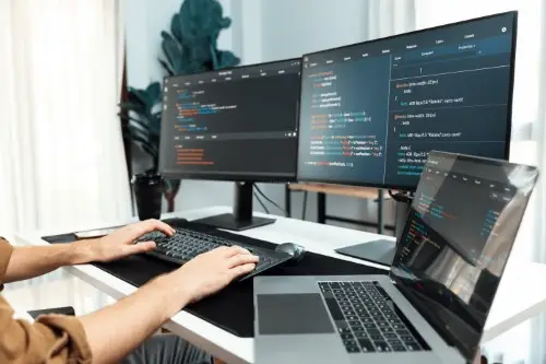 Programista siedzi przed ekranami na których jest kod programu